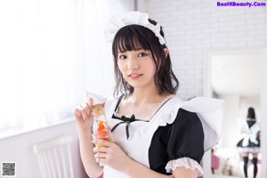 A woman in a maid outfit sitting on a pink couch.