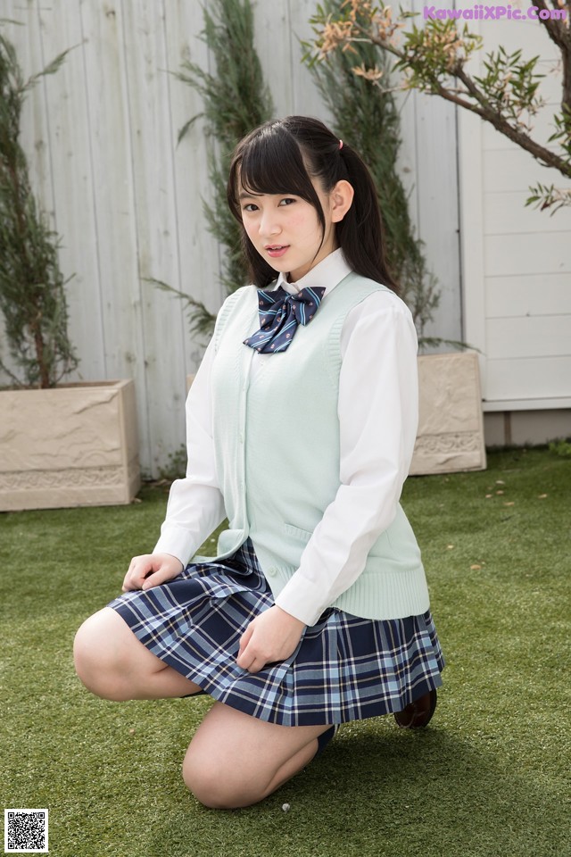 A young woman in a school uniform crouching on the grass.