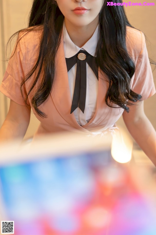 A woman in a pink shirt and black bow tie sitting at a table.