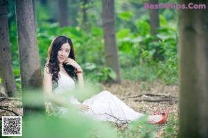 A woman in lingerie sitting on a leaf in the woods.