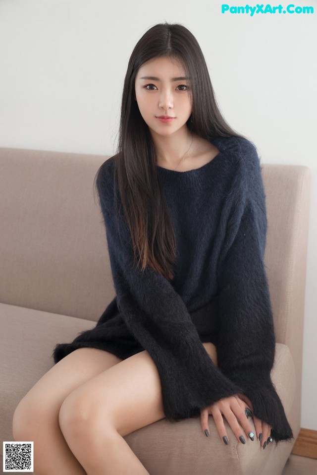 A woman sitting on a couch wearing a black sweater.