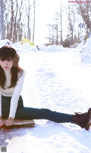 A young woman wearing a fur hat sitting on the ground.