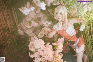 A woman in a kimono sitting on a rock in front of flowers.