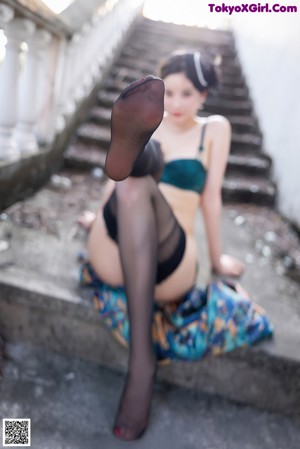 A woman in a blue dress and black stockings leaning on a railing.