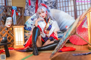 A woman in a kimono sitting on the floor with a fan.