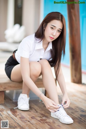 A woman sitting on a wooden bench wearing white shoes.