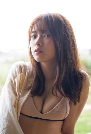 A woman in a white top and panties sitting on a bed.