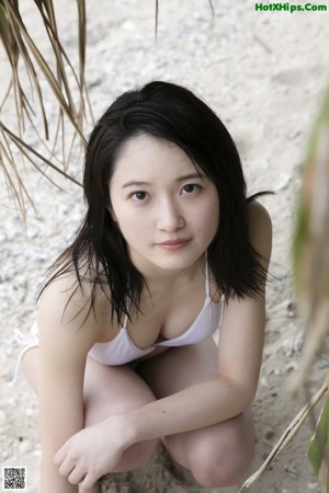 A woman in a beige dress sitting on a dirt road.