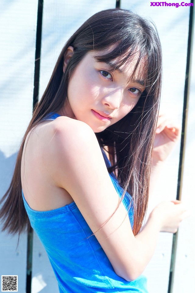 A woman in a blue tank top leaning against a fence.