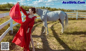 A woman standing next to a white horse in a field.