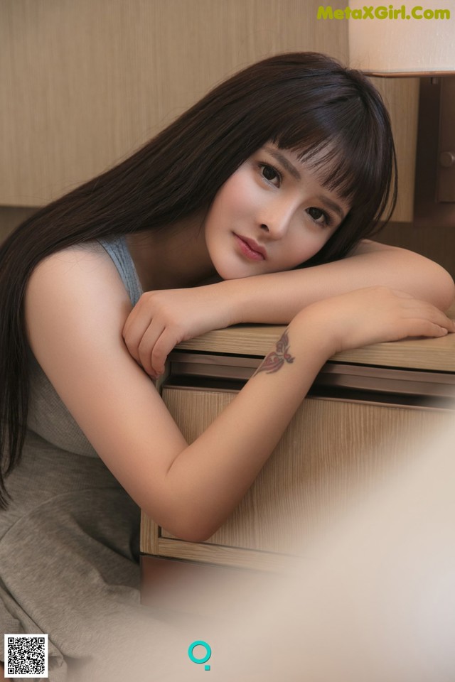 A woman with long black hair leaning on a dresser.