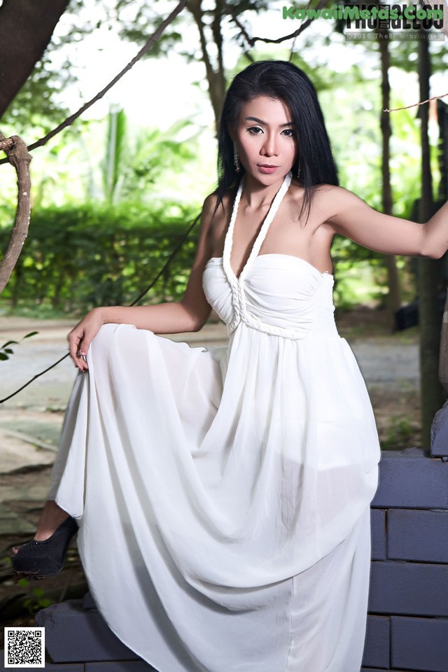 A woman in a white dress sitting on a stone wall.