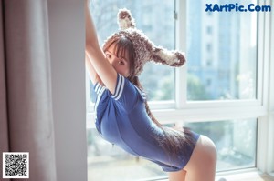 A woman in a blue dress sitting on a window sill.