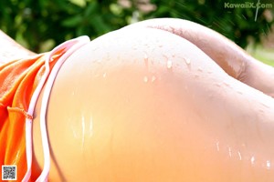 A woman in an orange top and blue shorts leaning against a tree.